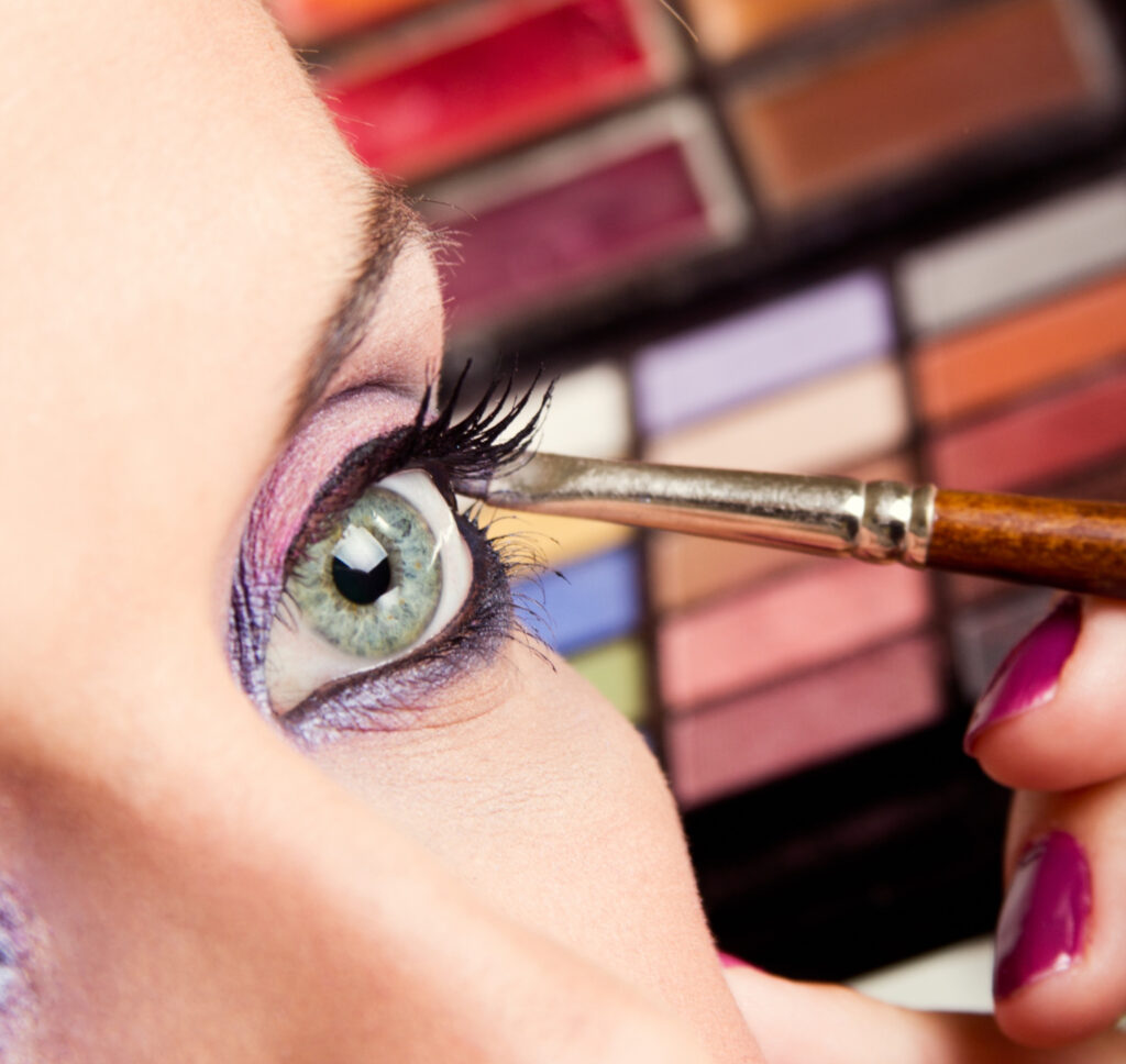Detalhe de mulher fazendo esfumado rosa e roxo nos olhos com pincel