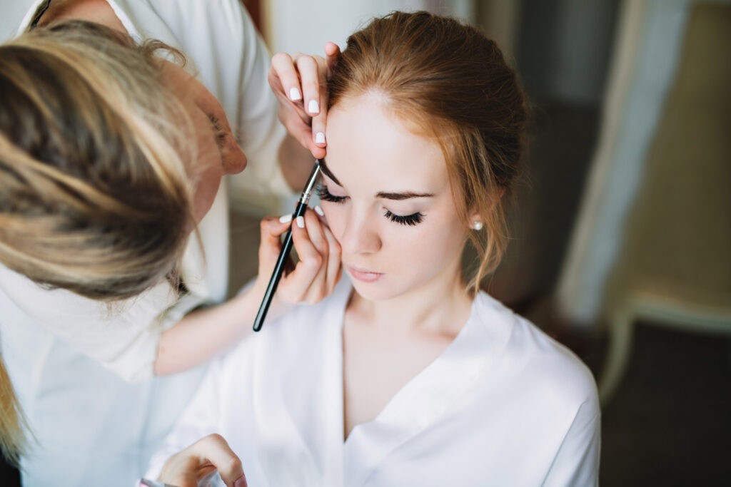 "Maquiadora profissional aplicando maquiagem delicada em noiva, preparando um look natural e duradouro para o dia do casamento."